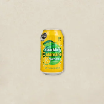Bright yellow can of Sparkling Calamansi drink with lime slices and leaves, centered on a light textured background.