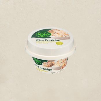 Bibigo Rice Porridge cup with mushrooms and vegetables on a beige background, front view with white lid