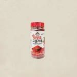Red-capped bottle of chili pepper powder with a Korean label, placed against a beige background, isolated image.