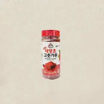 Red-capped bottle of chili pepper powder with a Korean label, placed against a beige background, isolated image.