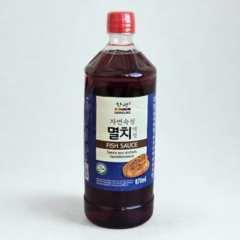 Brown glass bottle of fish sauce with a red cap; blue label shows Korean text and 'FISH SAUCE' with 870 ml printed on it.