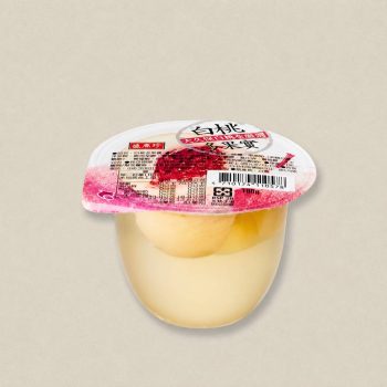 Individual yogurt cup with a white-pink lid and visible fruit chunks inside, set against a neutral background