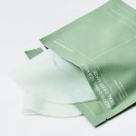 Green facial mask packaging opened to reveal a translucent sheet mask ready for use in a skincare routine