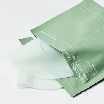 Green facial mask packaging opened to reveal a translucent sheet mask ready for use in a skincare routine