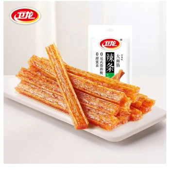 Plate of orange, crispy snack sticks stacked on a white dish with a white pouch featuring a red-and-yellow logo in the background (snack product shot).