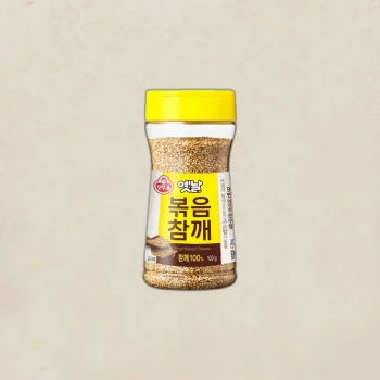 Jar of Ottogi roasted sesame seeds with a bright yellow lid and yellow label, 100 g weight shown on the label.